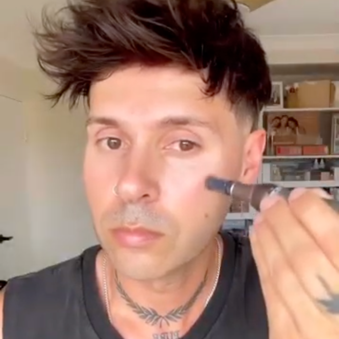 Close-up of one person with dark hair and a nose ring holding a dark gray microneedling pen to their right cheek.
