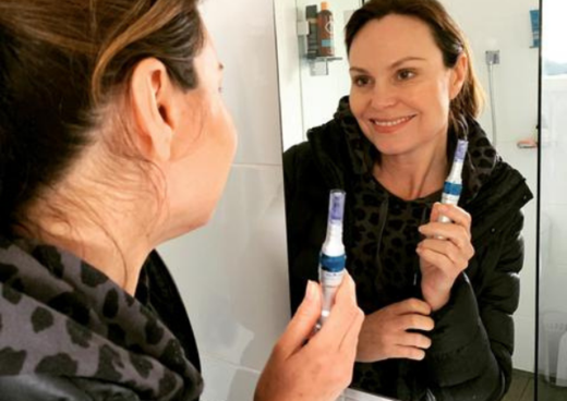 woman holding her dr pen microneelding pen whilst looking into the mirror