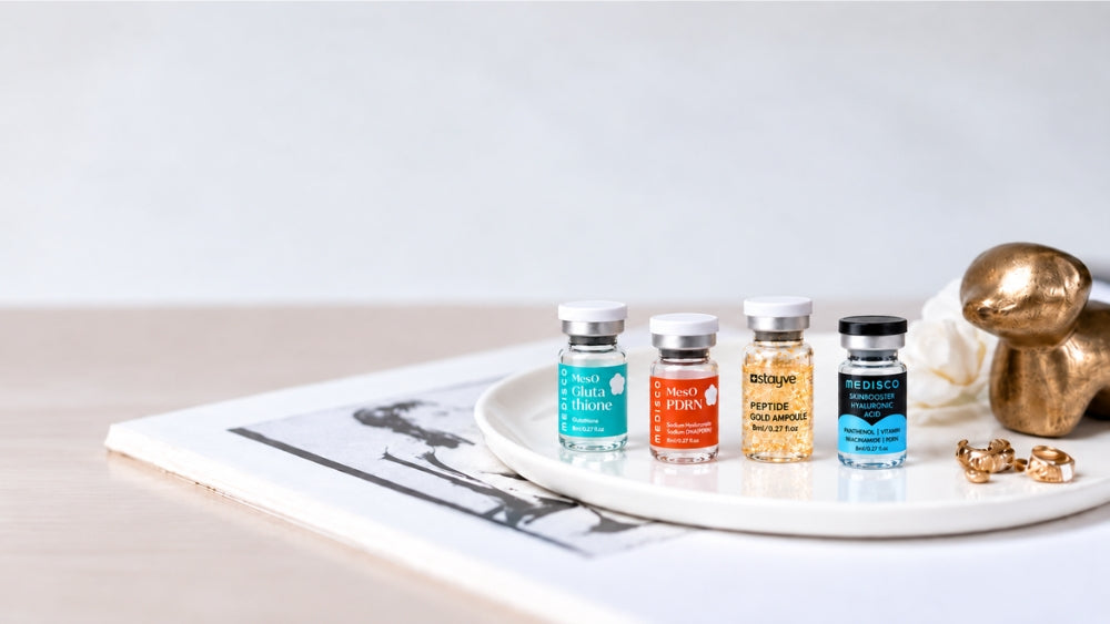 Four microneedling serum vials on a ceramic tray, including PDRN, glutathione, peptide gold and hyaluronic acid, for a blog on the best ampoules to use with microneedling.